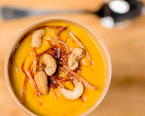 Thai Pumpkin Coconut Curry with cashew Soup in a takeaway container on a wooden background