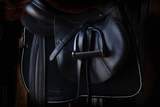 Shiny black leather horse saddle in the dark stable , with stirrup, ready for riding 