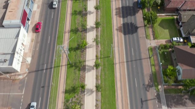 Aerial reveal of Melbourne city along main road with trams, palms, and bikes.