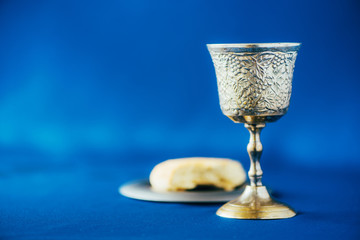 Communion still life. Unleavened bread, chalice of wine, silver kiddush wine cup on blue...