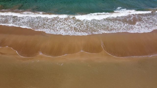 Olas rompen sobre la arena de la playa, mientras la c&aacute;mara comienza a descender en plano cenital, pero corrigiendo hasta ver el mar y la l&iacute;nea del horizonte al llegar casi a ras de suelo