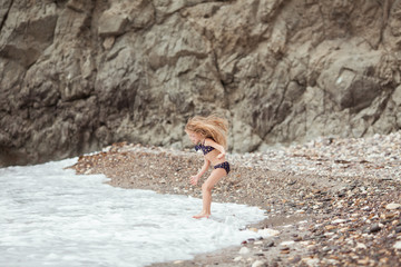 Happy pretty girl walks along the sea coast against the background of the sea, from behind a beautiful landscape