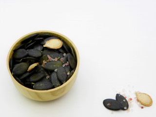 Pumpkin seeds with salt. Peeled pumpkin seeds in a wooden bowl close-up on a white background.    