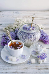 a Cup of tea and lilac with sugar on a wooden table