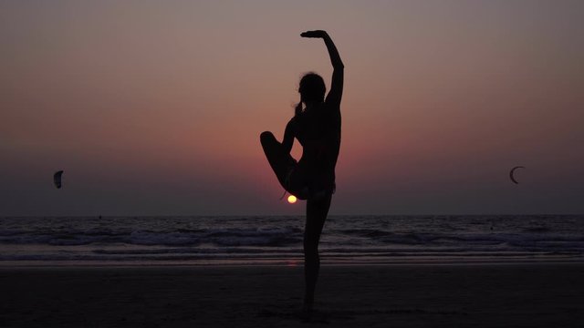 A woman practices yoga on the sea beach at sunset. Evening yoga and self-development