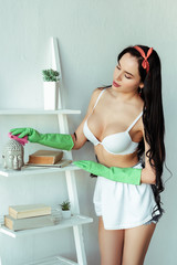 Obraz premium Seductive woman in rubber gloves cleaning decorative statuette on rack at home
