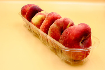  closeup of plastic  punnet of ripe fresh fruit  flat peaches in a row isolated with nobody