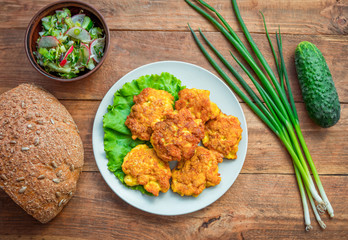 Homemade chicken patties, served on a plate, salad, bread, green onion and cucumbers on wooden table