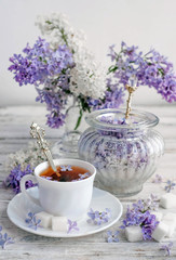 a Cup of tea and lilac with sugar on a wooden table