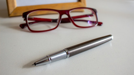 Fototapeta premium Metal pen, beautiful glasses and frame on a white table. Business concept.
