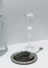 black caviar on a beautiful silver plate with small silver fork next to a bottle of vodka and short glass full of vodka