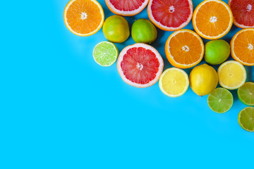 Blue background with different sliced citrus - oranges, grapefruits, lemons and limes. Flat layout with space for text