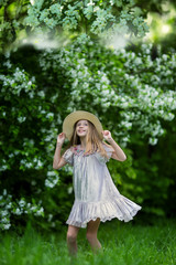 Adorable little girl in a hat in a blooming apple tree garden on a beautiful spring day. Cute child picking fresh apple tree flowers at spring.