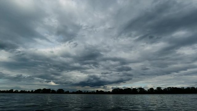 Time Lapse view of the river and the clouds running above it before the rain, dark blue and the forest opposite