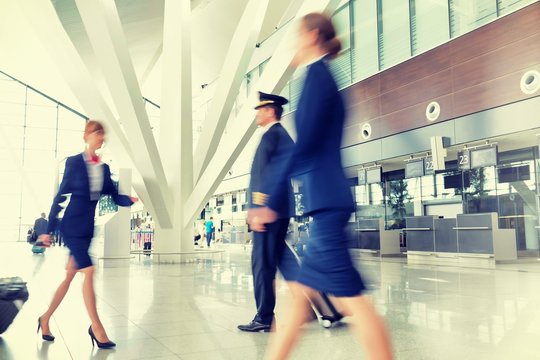 Mature pilot with young beautiful flight attendants walking in airport
