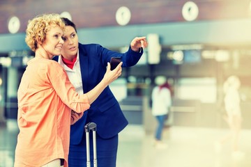 Portrait of mature woman showing her smartphone while airport staff pointing direction
