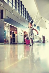Portrait of young adorable little girl running in airport with her pink suitcase

