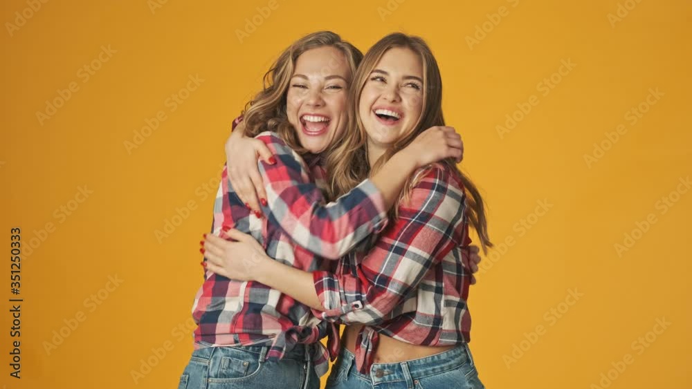 Sticker young positive girls friends sisters isolated over yellow wall background hugging