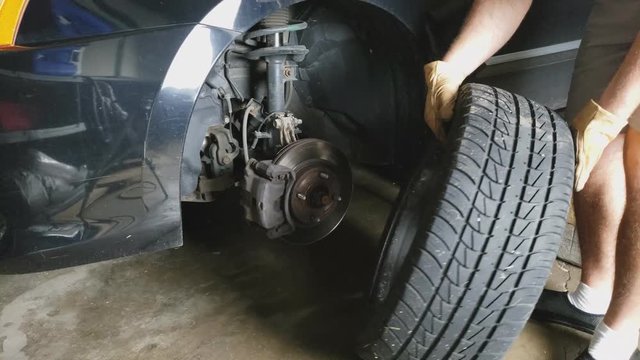 Removing front left wheel and tire from sedan car exposing axle assembly with brakes and rotor disk preparing for some repairs in garage.