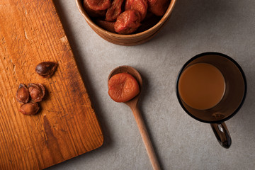 Dried apricots on wooden spoon and round wooden box. Cup of tea with milk. Apricots kernels on old wooden kitchen board. Tea time, organic tasty and healthy diet food concept photo.