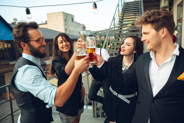 Success. Young people celebrating, look happy, have party at office or bar. Men and women drinking alcohol, talking, laughting. Holidays, weekend, business and finance, friendship concept