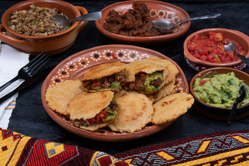 Vegan Mexican gorditas along with refried beans, guacamole, tomato salsa and fried seitan pieces in traditional Mexican bowls