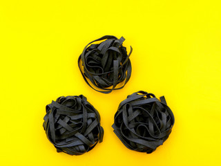 Tagliatelle pasta with cuttlefish ink on a yellow background         