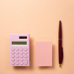 Work and study place, memo pad and digital calculator and pen on beige pink background. flat lay, top view, copy space