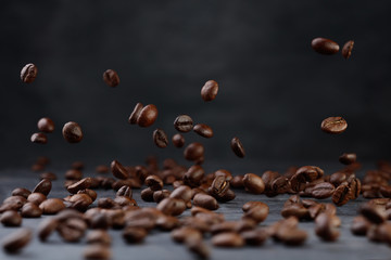 Many roasted coffee beans flying/falling in the air. Selective focus. Сoffee beans on a background of gray stone wall and table