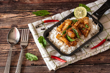 Stir fried crispy pork with basil and steam rice on tray as Thai culture street food on wooden table 