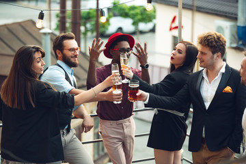 Young people celebrating, look happy, have party at office or bar. Men and women drinking alcohol, talking, laughting. Holidays, weekend, business and finance, friendship concept. Teambuilding.