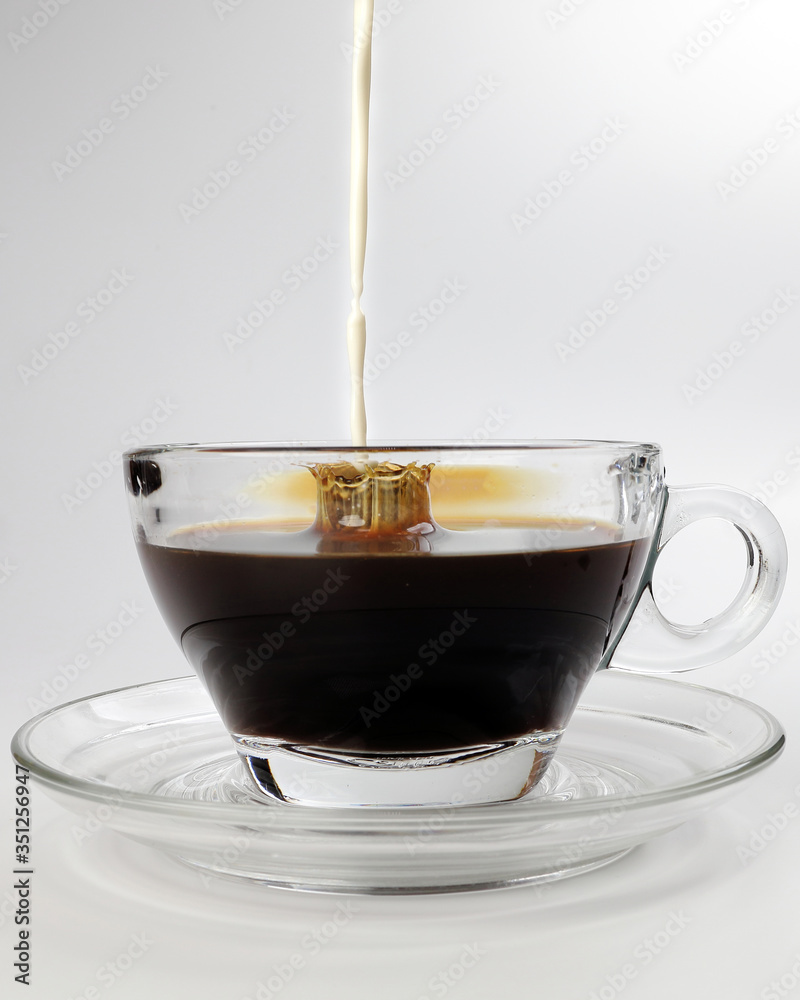 Wall mural dark coffee poring white milk dripping splash shadow liquid swirl in glass cup saucer on white backg