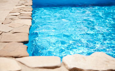 Fototapeta na wymiar Relax by the pool at home with clear blue water. The deep pool is lined with decorative stone at the edge, the sun is reflected in the water with a sparkle