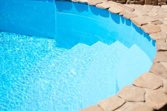 A great summer day by the pool at home with clear blue water. A deep pool on the edge of the overlaid decorative stone, photo horizontal background, commercial swimming pools hotels