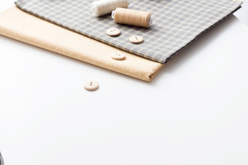 Sewing tools on a white background. A set of fabrics with a pattern, threads, buttons, scissors. sewing workshop atelier for sewing clothes. Flat layout, copy space.