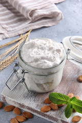 Fermented milk product. Healthy yogurt with cereals in a transparent jar on a white wooden board with nuts, mint and ears on a light grey background. Background image, copy space