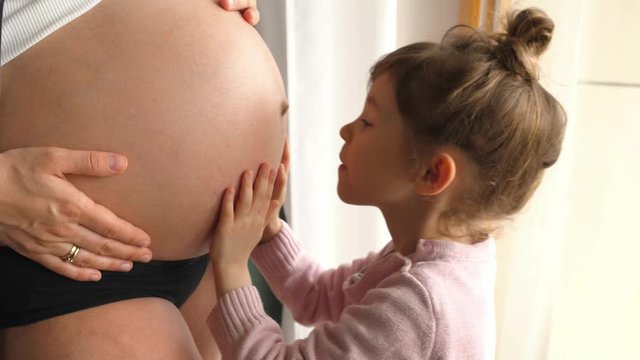 girl older sister kissing hugging pregnancy belly, smiling looking 