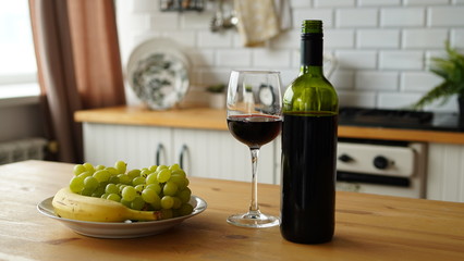 Close up of open bottle of wine and glass of wine with fruits on plate on table in kitchen. Concept of dating.