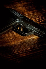 Shabby old gun on a brown table. Black weapon on a wooden board close up. Weapon on a dark background with contrasting dramatic light.