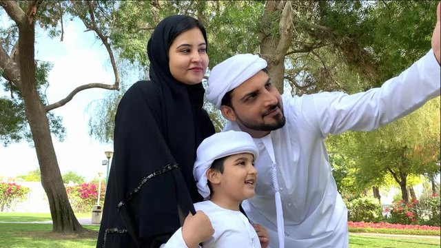 Arab Emirati Father doing selfie for this family wearing Kandura and Abaya. UAE locals taking family photo at an outdoor location during day time. Happiness concept