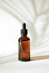Naklejka premium Glass bottle with moisturizing serum. Brown bottle with a dropper on a background of tropical shadow of a palm leaf. The concept of skin care