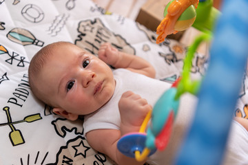 Adorable little baby boy lying on his back surrounded by colourful toys