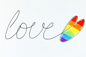 The word Love is written in black marker with a heart painted in the colors of the Lgbt flag rainbow heart shape on white. Concept of the Pride day, Valentine day, freedom, love.