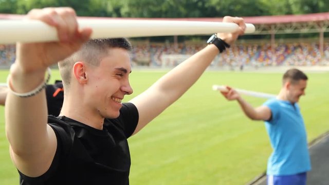 Sportive man, using pilates exercise body stick or bar while having workout at stadion.