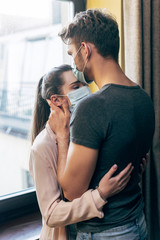 man in medical mask kissing forehead of woman at home