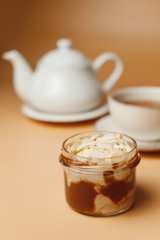 Mousse with caramel and almond petals, a teapot and a cup of tea on an orange background