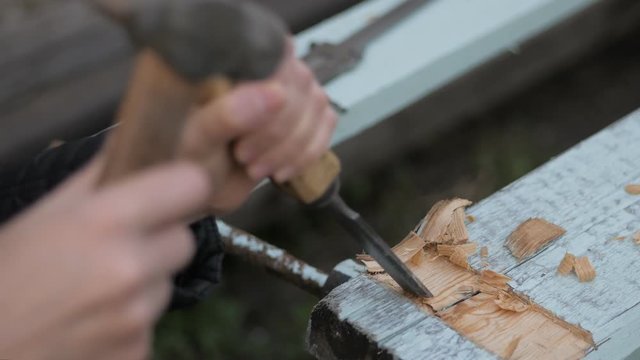 Close-up of an adult woman working with a hammer and chisel on a wooden surface.
