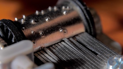Music box drum clockwork mechanism close up on turning barrel and cogs. Old music box mechanism, rotating cylinder closeup. Toy barrel organ rotates, closeup view at orange background