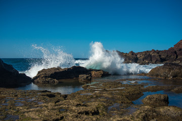 the rocky seaside of Lanzarote island with crashing waves on a sunny day with a blue sky 