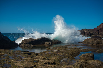 the rocky seaside of Lanzarote island with crashing waves on a sunny day with a blue sky 